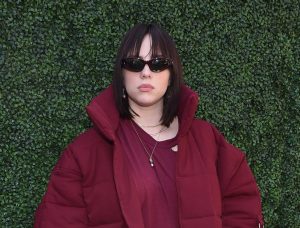 Billie Eilish mit schwarzer Sonnenbrille und roter Oversize-Jacke.